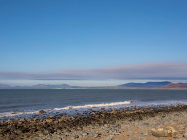 A rocky shoreline with ocean waves and mountains in the distance at Allt y Mor in Harlech