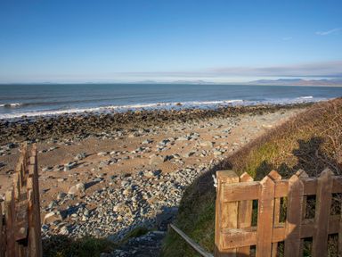 A rocky beach with a wooden fence and steps leading down to the shore at Allt y Mor in Harlech