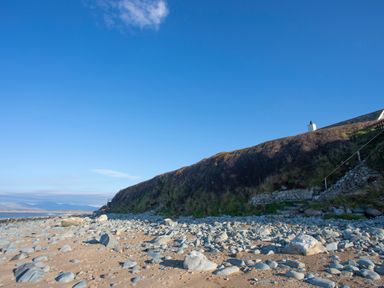 A rocky beach with a grassy cliff and a chimney visible at the top at Allt y Mor in Harlech
