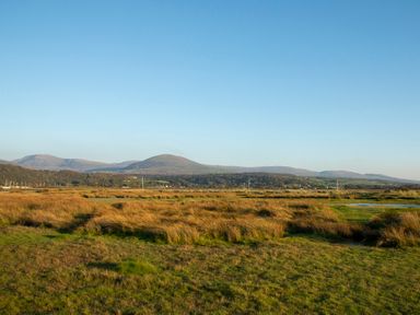 A grassy field with hills in the background under a clear blue sky at Allt y Mor in Harlech