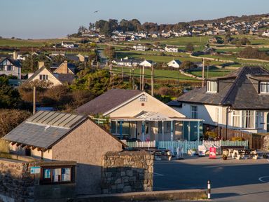 A cafe with outdoor seating and houses on green hills in the background at Allt y Mor in Harlech