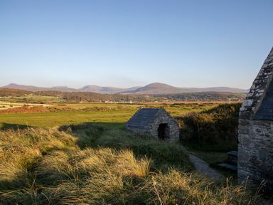 An outdoor landscape with grassy fields stone structures and mountains in the background at Allt y Mor in Harlech