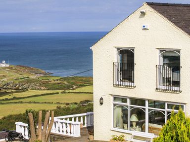 A house with white walls and black railings near the coast with green fields and a body of water at Amolca in Llaneilian