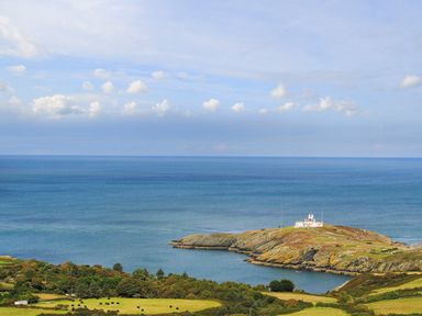 A coastal landscape with a lighthouse on a small peninsula surrounded by the sea and fields at Amolca in Llaneilian