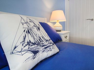 A pillow with a sailing ship design on a blue bed with a lamp on a bedside table in a bedroom at Amolca in Llaneilian