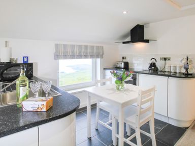 A kitchen with a small white dining table and chairs flowers on the table window with a view kitchen appliances on counters at Amolca in Llaneilian