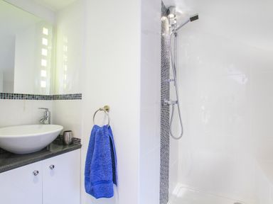 A bathroom with a white sink on a black countertop a blue towel hanging a walk in shower with a showerhead and white tiles at Amolca in Llaneilian