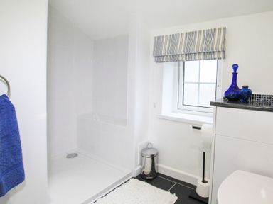 A bathroom with a walk in shower a window with striped blind and blue glass bottles on the counter at Amolca in Llaneilian