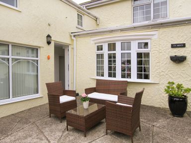 An outdoor patio with four wicker chairs and a glass table with a flower pot at Amolca in Llaneilian
