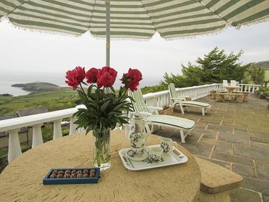 A patio table with flowers and tea set under a striped umbrella with lounge chairs and a sea view at Amolca in Llaneilian