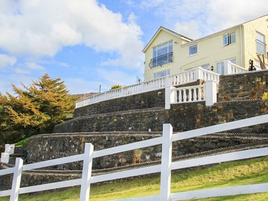 A multi level stone terrace with white railings and a cream house in the background at Amolca in Llaneilian
