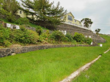 A house on a hill with stone retaining walls green grass and shrubs at Amolca in Llaneilian
