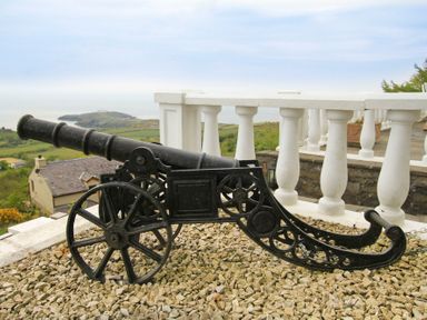 A black decorative cannon on gravel with a white balustrade and scenic countryside and sea in the background at Amolca in Llaneilian