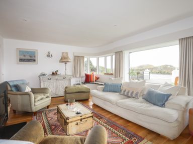 A living room with beige sofas armchairs a patterned rug wooden floor and large windows at Angorfa - Trearddur Bay in Trearddur Bay