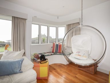 A living room with a hanging bubble chair and a curved bench by the window at Angorfa - Trearddur Bay