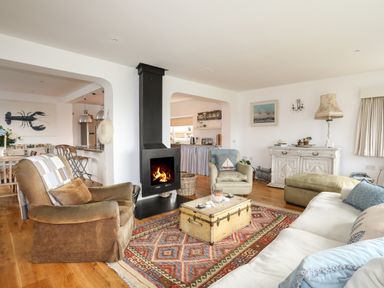 A living room with a fireplace armchairs a sofa a patterned rug and a wooden chest at Angorfa - Trearddur Bay