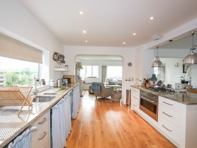 A kitchen with wooden floors and a view into a living area at Angorfa Trearddur Bay