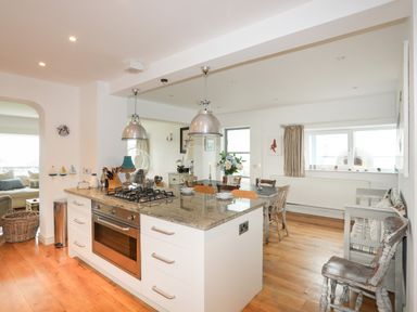 A kitchen island with stove and oven next to a dining table with chairs and flowers at Angorfa - Trearddur Bay
