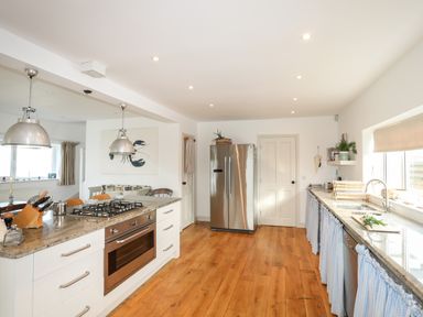 A kitchen with wooden floor white cabinets stainless steel fridge and stove at Angorfa - Trearddur Bay in Trearddur Bay