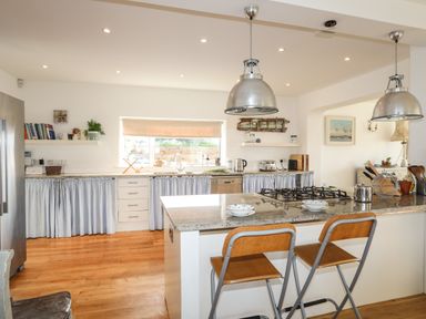 A kitchen with an island, gas stove, two chairs, shelves with books and kitchen appliances at Angorfa - Trearddur Bay