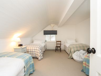 A bedroom with three single beds a bedside table with a lamp a wooden chair and a window at Angorfa - Trearddur Bay