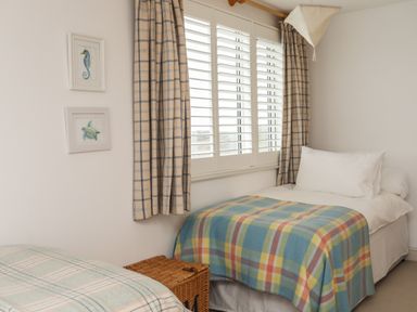 A bedroom with two single beds a wicker basket plaid blankets curtains and framed sea creature pictures on the wall at Angorfa Trearddur Bay