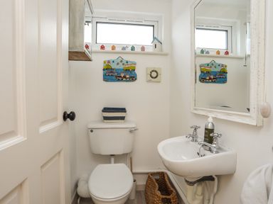 A small bathroom with a toilet sink mirror and decorative items at Angorfa - Trearddur Bay