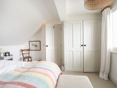 A bedroom with a striped blanket on the bed a chair a framed picture and white closet doors at Angorfa - Trearddur Bay in Trearddur Bay