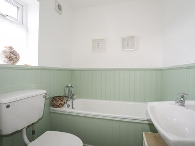 A bathroom with a toilet sink and bathtub with green paneling and white walls at Angorfa - Trearddur Bay