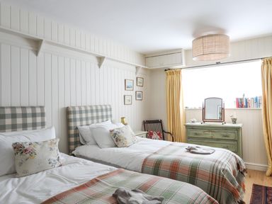 A bedroom with two single beds plaid headboards floral pillows a green dresser with a mirror and yellow curtains at Angorfa - Trearddur Bay in Trearddur Bay