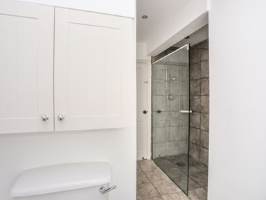 A bathroom with a toilet, white cabinets, and a glass shower enclosure with tiled walls at Angorfa - Trearddur Bay in Trearddur Bay