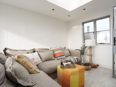 A seating area with a sectional sofa, colorful cushions, a patterned ottoman, a wooden tray with teacups, a floor lamp, and two plants at Angorfa - Trearddur Bay in Trearddur Bay