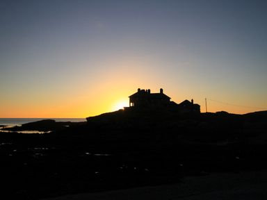 A silhouette of a house on a rocky coastline at sunset with the sea in the background at Angorfa - Trearddur Bay in Trearddur Bay