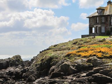 A stone house on a rocky coastal cliff with stairs leading up to it at Angorfa Trearddur Bay