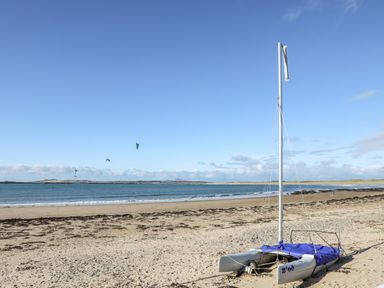 A catamaran sailboat on a sandy beach with sea and kite surfers in the background at Arkoo in Rhosneigr