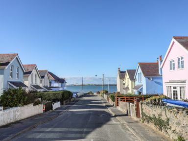 A residential street with pastel colored houses leading to a body of water at Arkoo in Rhosneigr