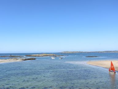 A coastal scene with boats on clear water and a person near a small red sailboat at Arkoo in Rhosneigr