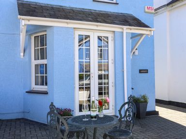 A blue exterior wall with white framed glass doors and windows and a metal table with two chairs on a paved area at Arkoo in Rhosneigr