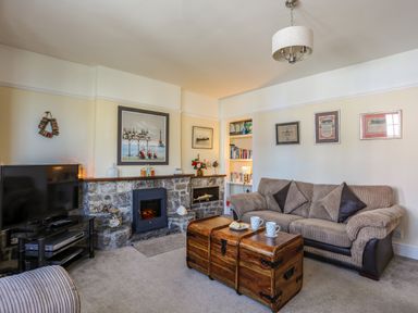 A living room with a sofa and wooden chest coffee table by a stone fireplace and a television at Arkoo in Rhosneigr