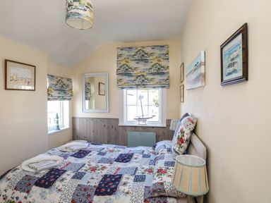 A bedroom with a patterned bedspread two windows with printed blinds artworks on walls and two bedside lamps at Arkoo in Rhosneigr
