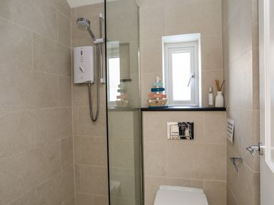 A bathroom with a shower area a small window and a toilet at Arkoo in Rhosneigr