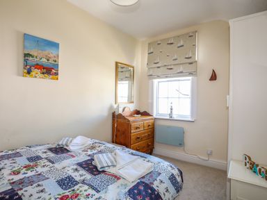 A bedroom with a bed a wooden dresser a window with patterned blinds and a painting on the wall at Arkoo in Rhosneigr