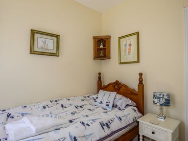 A bedroom with a wooden bed with boat patterned bedding a white bedside table and framed pictures on the walls at Arkoo in Rhosneigr
