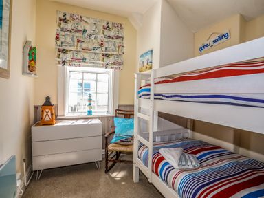 A bedroom with a white bunk bed with striped bedding and a white dresser under a window with a sailboat curtain at Arkoo in Rhosneigr