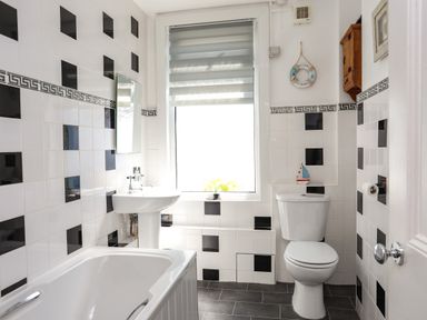 A bathroom with a bathtub a sink a toilet and a window with a blind at Arkoo in Rhosneigr