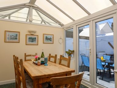 A dining area with a wooden table and chairs next to glass doors leading to a patio with blue chairs at Arkoo in Rhosneigr