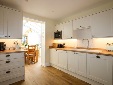 A kitchen with white cabinets wooden countertops and a dining area with wooden chairs at Arkoo in Rhosneigr