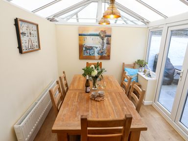 A dining room with a wooden table and chairs a glass roof and two pendant lights at Arkoo in Rhosneigr