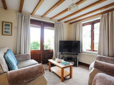 A living room with sofas a wooden coffee table a television and a door with windows at Barras Cottage in Brynsiencyn