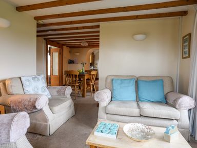 A living room with two beige sofas with blue cushions a wooden coffee table and a wooden dining table with chairs at Barras Cottage in Brynsiencyn